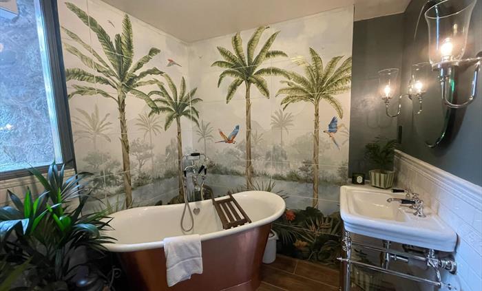 The family bathroom in the west wing of Ysgubor Degwm seadog and stone. A copper bath with white enamel inside, mural wall and wooden floor.